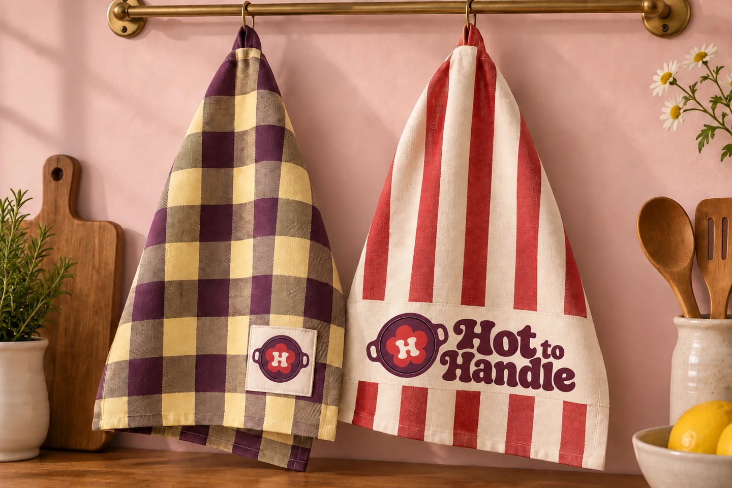 Plum-and-butter checked tea towel with an upright pan patch beside a cherry-striped towel with the tilted-pan Hot to Handle logo